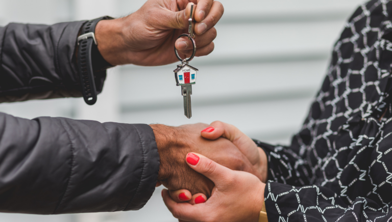 a pair of hands belonging to an older male gives a set of house keys to a younger pair of female hands, as though a house has been gifted from one generation to another.