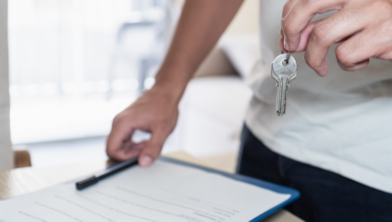A person holds a set of keys above a property rental agreement on a clipboard, symbolising a property handover or tenancy agreement.