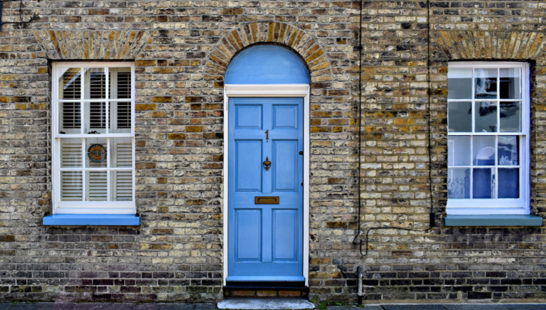 Blue front door and sash windows on a traditional British brick terraced house, featuring white window frames and a decorative arched doorway.
